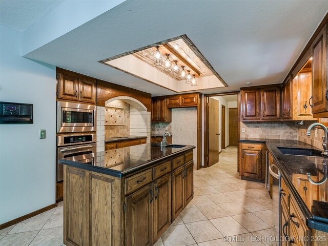 8934 S 41st W Ave, Tulsa, OK 74132 - kitchen with stainless steel appliances, decorative backsplash, light tile patterned floors, dark stone counters, and a center island with sink