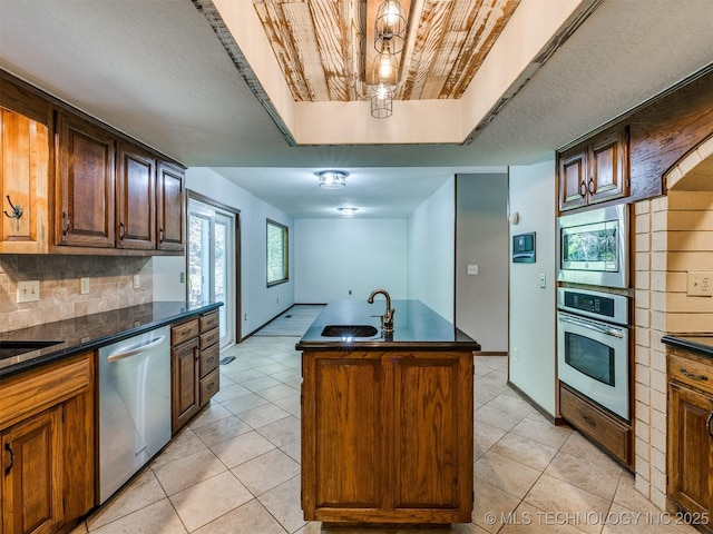 8934 S 41st W Ave, Tulsa, OK 74132 - kitchen featuring stainless steel appliances, dark countertops, light tile patterned floors, tasteful backsplash, and an island with sink