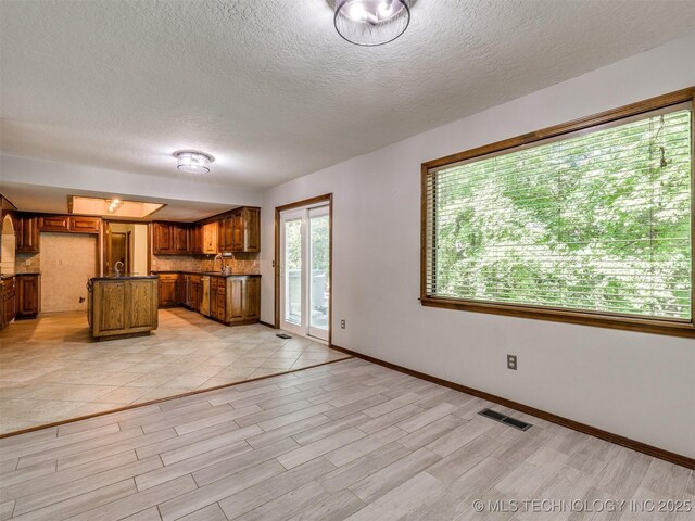 8934 S 41st W Ave, Tulsa, OK 74132 - kitchen featuring dark countertops, brown cabinets, light wood-style floors, a textured ceiling, and an island with sink