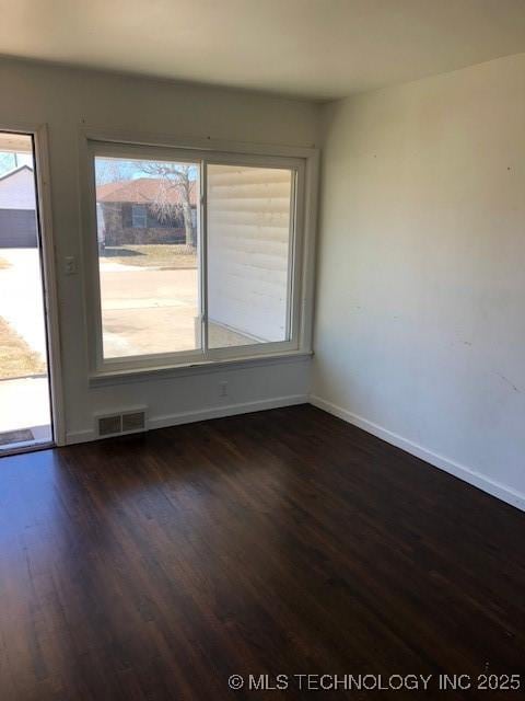 empty room with dark wood-style flooring, visible vents, and baseboards