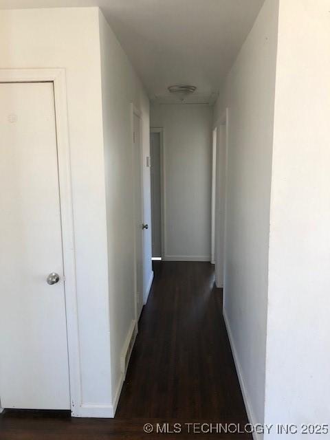 corridor featuring baseboards and dark wood-type flooring