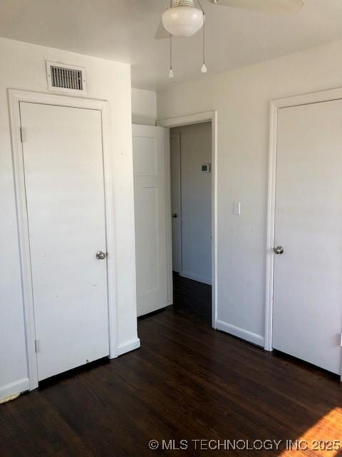 unfurnished bedroom with a ceiling fan, dark wood-style flooring, visible vents, and baseboards