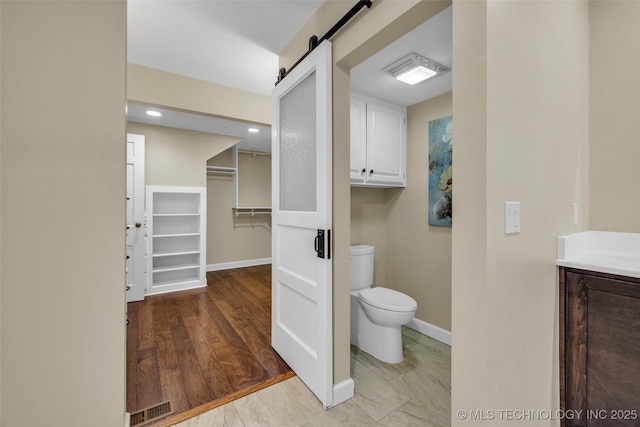 bathroom featuring visible vents, toilet, vanity, wood finished floors, and baseboards