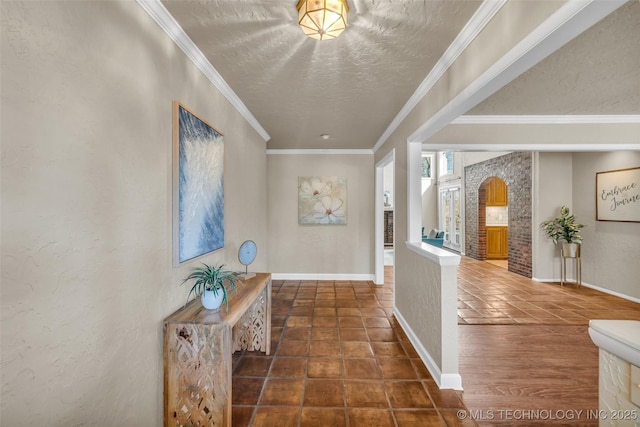 hall featuring a textured ceiling, a textured wall, ornamental molding, and baseboards