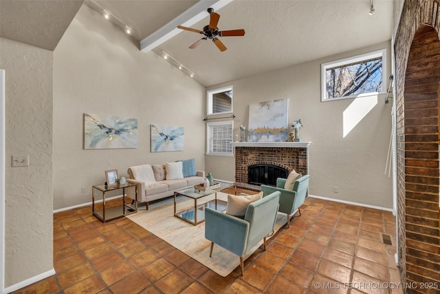 living room featuring beam ceiling, a textured wall, a ceiling fan, a brick fireplace, and baseboards