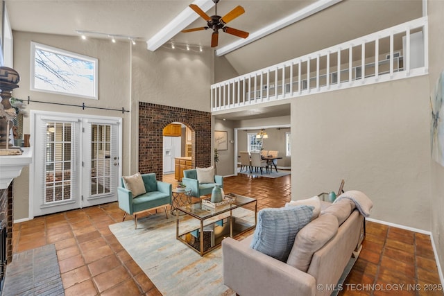 living area featuring arched walkways, high vaulted ceiling, a fireplace, a ceiling fan, and beamed ceiling