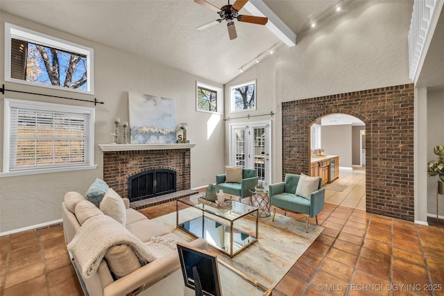 living area featuring arched walkways, a textured wall, a brick fireplace, high vaulted ceiling, and baseboards