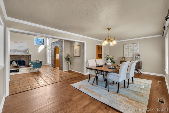 dining room with visible vents, wood finished floors, a textured ceiling, a fireplace, and a notable chandelier