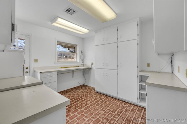 kitchen featuring brick floor, light countertops, white cabinets, and visible vents