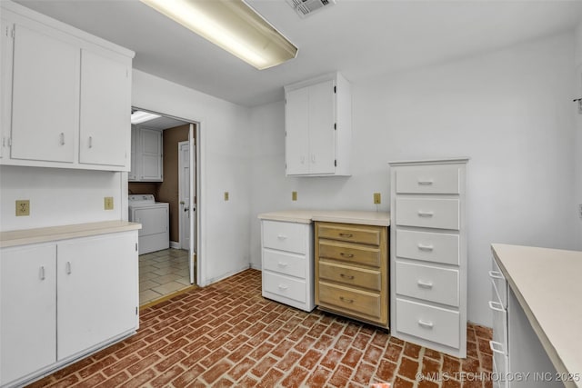 kitchen with visible vents, white cabinets, brick floor, light countertops, and separate washer and dryer