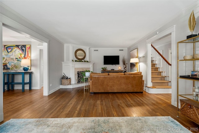 living area featuring a fireplace with raised hearth, crown molding, stairway, and wood finished floors