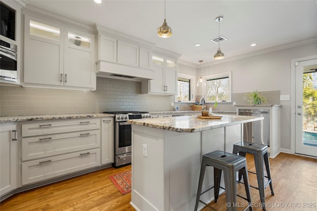 kitchen with appliances with stainless steel finishes, a breakfast bar area, ornamental molding, light wood-type flooring, and white cabinetry