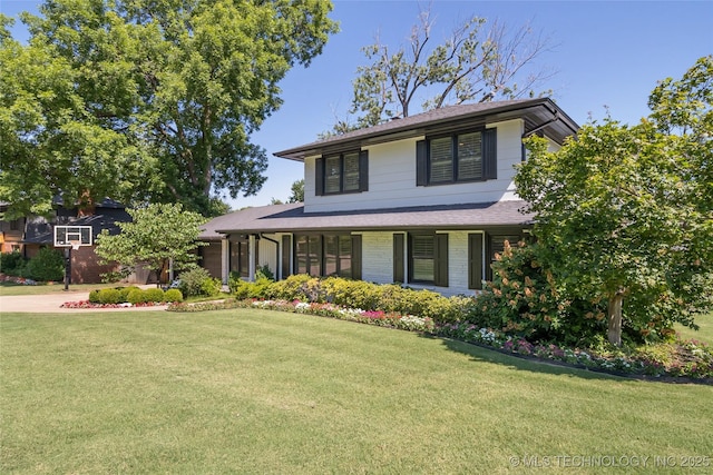 view of front of home with brick siding, roof with shingles, and a front yard