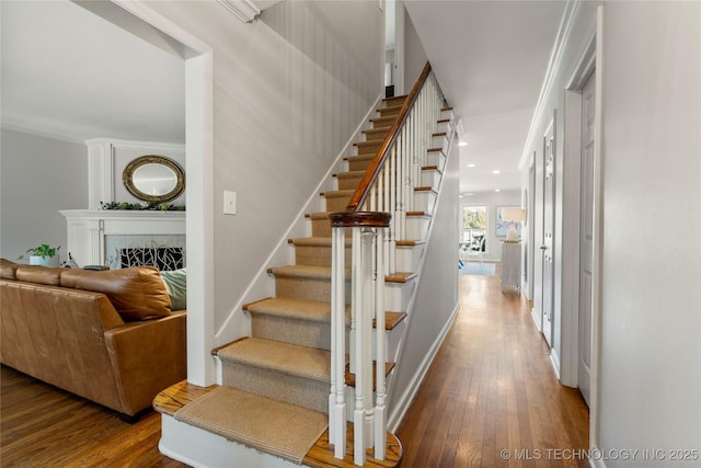 staircase with crown molding, hardwood / wood-style floors, a fireplace, and baseboards