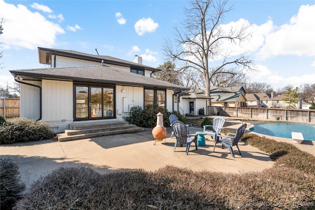 rear view of property featuring a fenced in pool, roof with shingles, a patio, a chimney, and fence