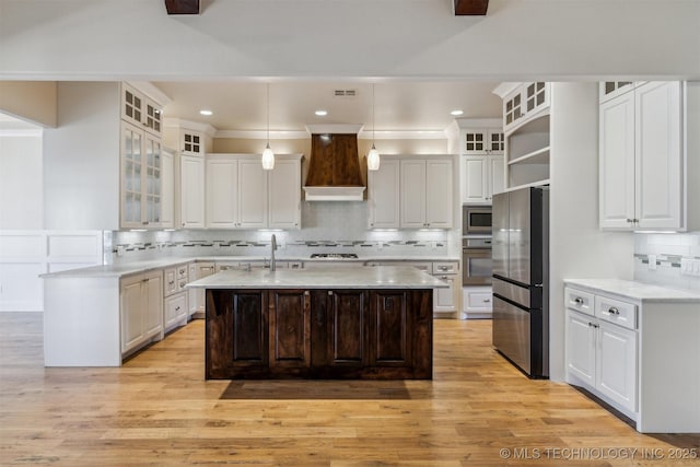 kitchen with stainless steel appliances, custom exhaust hood, a center island with sink, and white cabinetry