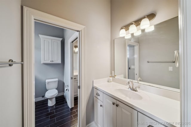 bathroom with toilet, vanity, baseboards, and wood finish floors