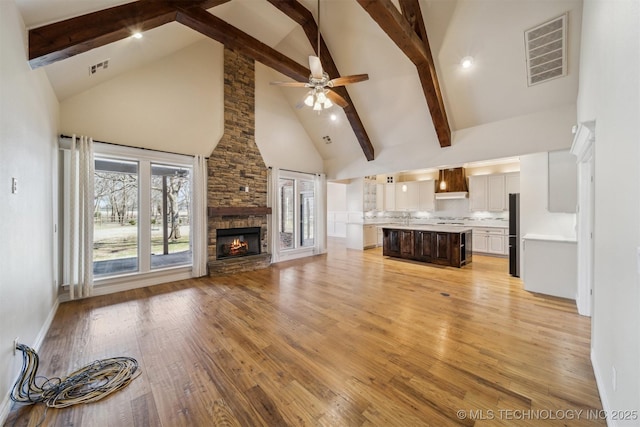 unfurnished living room featuring ceiling fan, high vaulted ceiling, a stone fireplace, visible vents, and light wood-type flooring