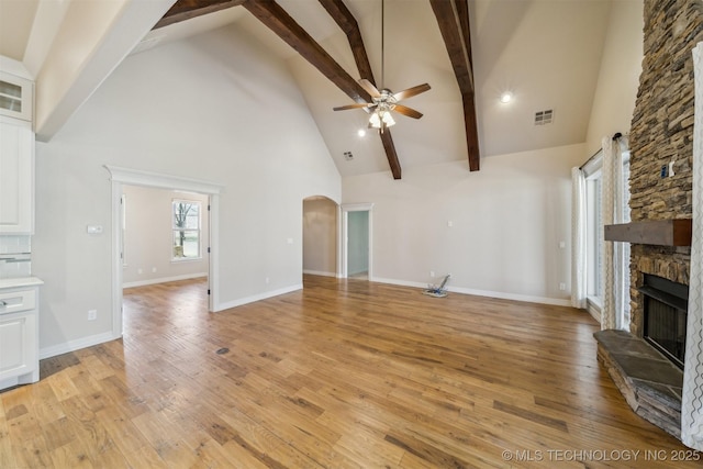 unfurnished living room featuring visible vents, arched walkways, ceiling fan, light wood-style flooring, and a stone fireplace