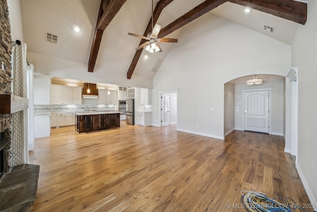 unfurnished living room with ceiling fan, arched walkways, light wood-style flooring, a large fireplace, and visible vents