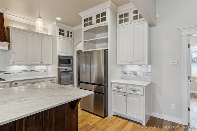 kitchen featuring stainless steel appliances, white cabinets, hanging light fixtures, light wood-type flooring, and decorative backsplash