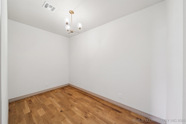 spare room featuring baseboards, visible vents, light wood finished floors, and an inviting chandelier