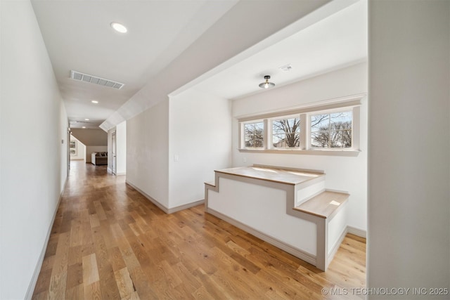 corridor with light wood-type flooring, visible vents, and baseboards