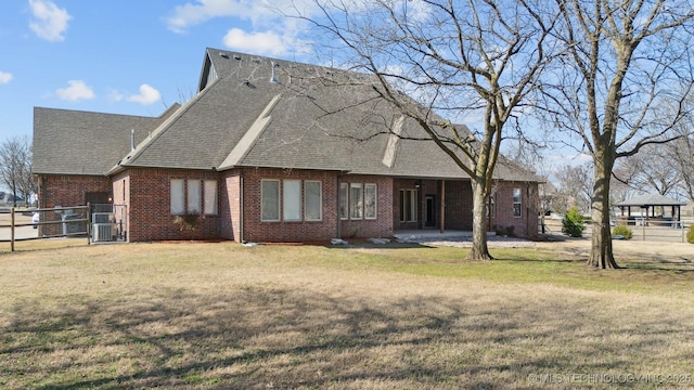 rear view of house featuring brick siding, a yard, and fence