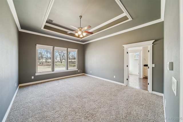 carpeted empty room with ornamental molding, a tray ceiling, visible vents, and baseboards