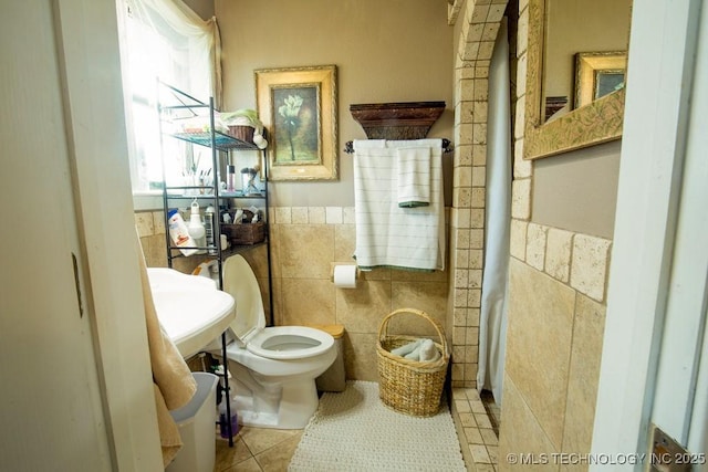 bathroom featuring tile walls, wainscoting, toilet, tile patterned flooring, and a sink