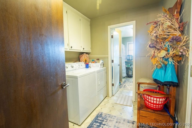 clothes washing area with cabinet space, wainscoting, light floors, and washing machine and clothes dryer