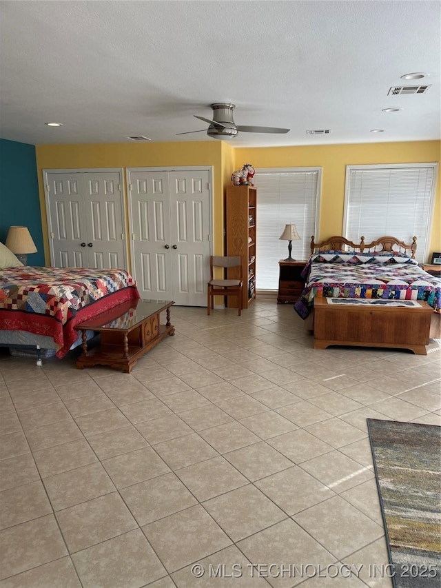 tiled bedroom featuring multiple closets, visible vents, a textured ceiling, and a ceiling fan