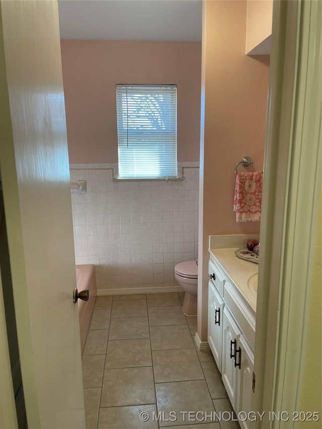 full bathroom with tile patterned flooring, toilet, vanity, tile walls, and wainscoting