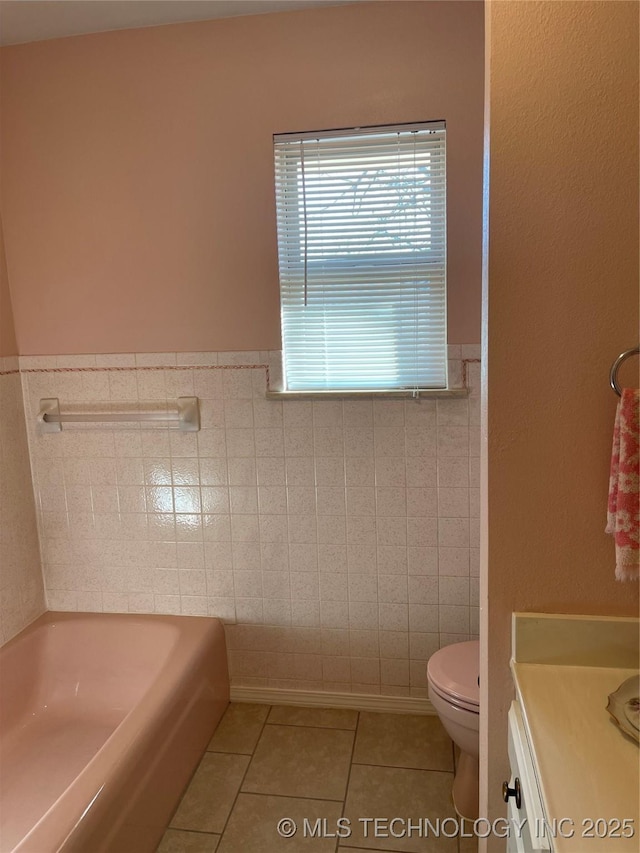 bathroom featuring wainscoting, toilet, tile patterned flooring, a washtub, and tile walls