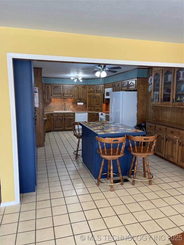 kitchen with decorative backsplash, a sink, ceiling fan, white appliances, and a kitchen breakfast bar