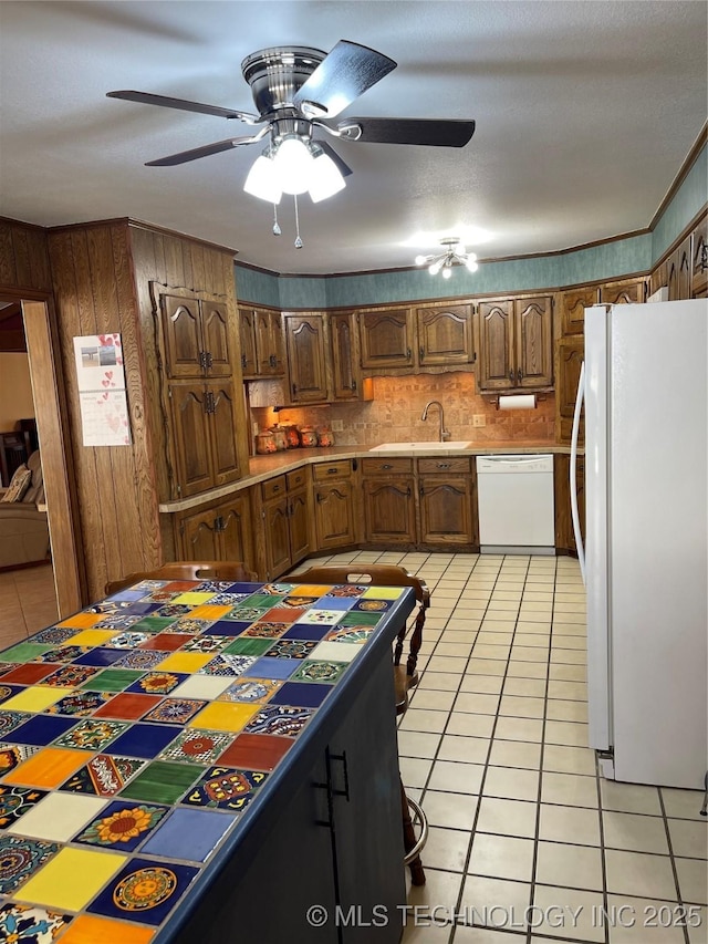 kitchen featuring white appliances, light tile patterned floors, brown cabinets, wood walls, and a sink