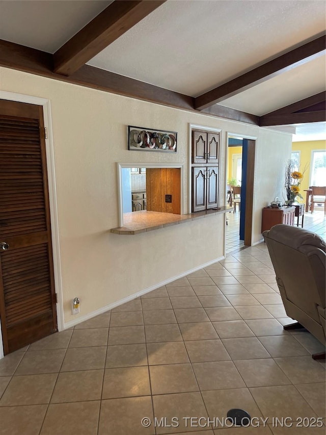 interior space featuring tile patterned flooring, baseboards, and beam ceiling