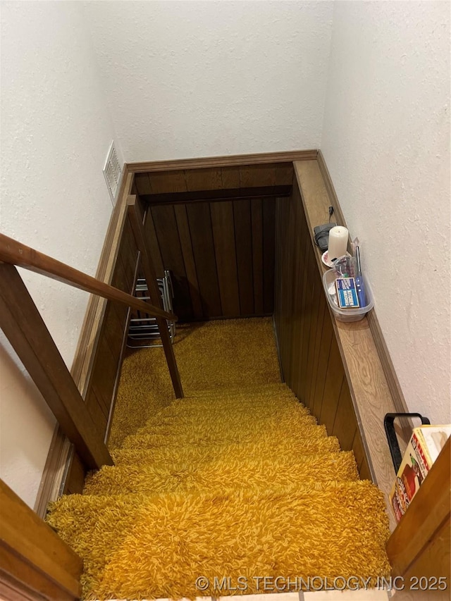 stairs with carpet floors, visible vents, and a textured wall