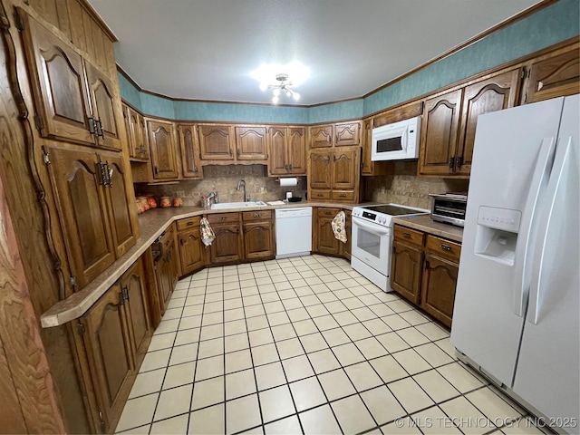 kitchen featuring white appliances, decorative backsplash, brown cabinets, crown molding, and a sink