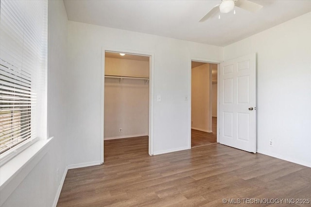 unfurnished bedroom with a walk in closet, a closet, baseboards, and wood finished floors