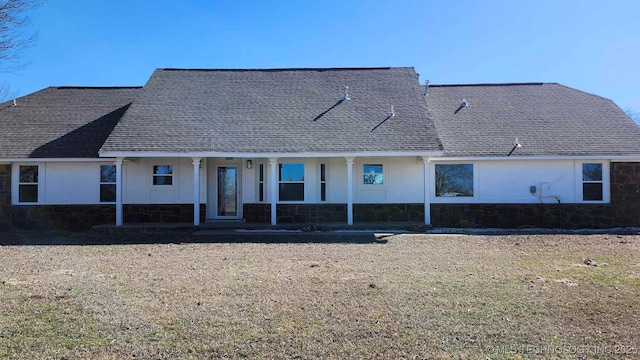 view of front of house featuring stone siding, a porch, roof with shingles, and a front yard