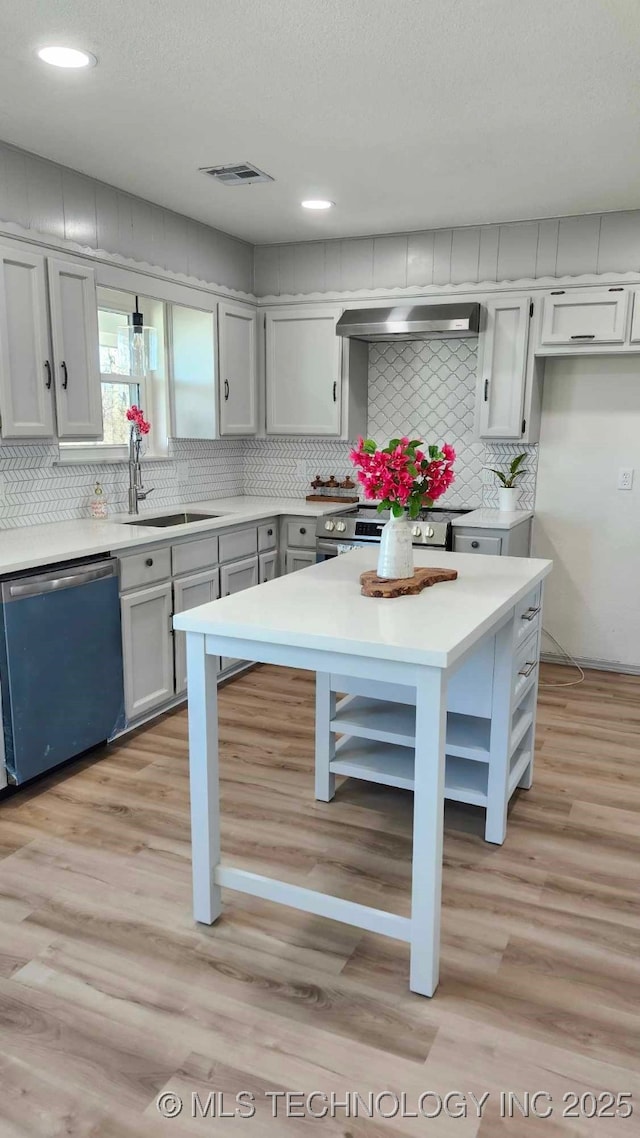 kitchen featuring dishwashing machine, light wood-style flooring, light countertops, wall chimney range hood, and open shelves