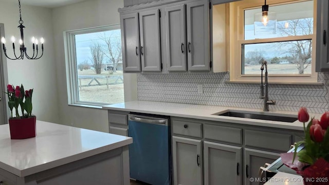 kitchen featuring dishwashing machine, hanging light fixtures, gray cabinets, light countertops, and a sink