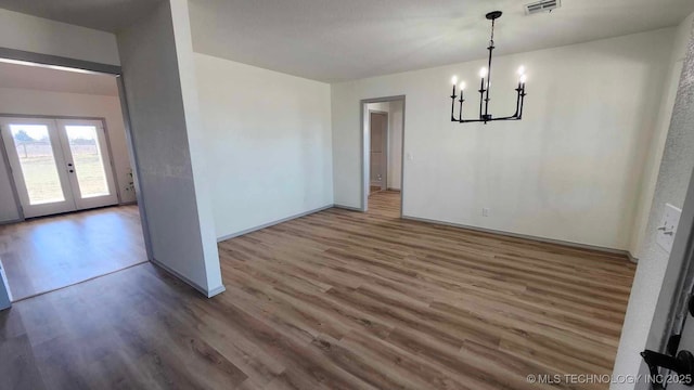 unfurnished dining area with a notable chandelier, visible vents, wood finished floors, and french doors