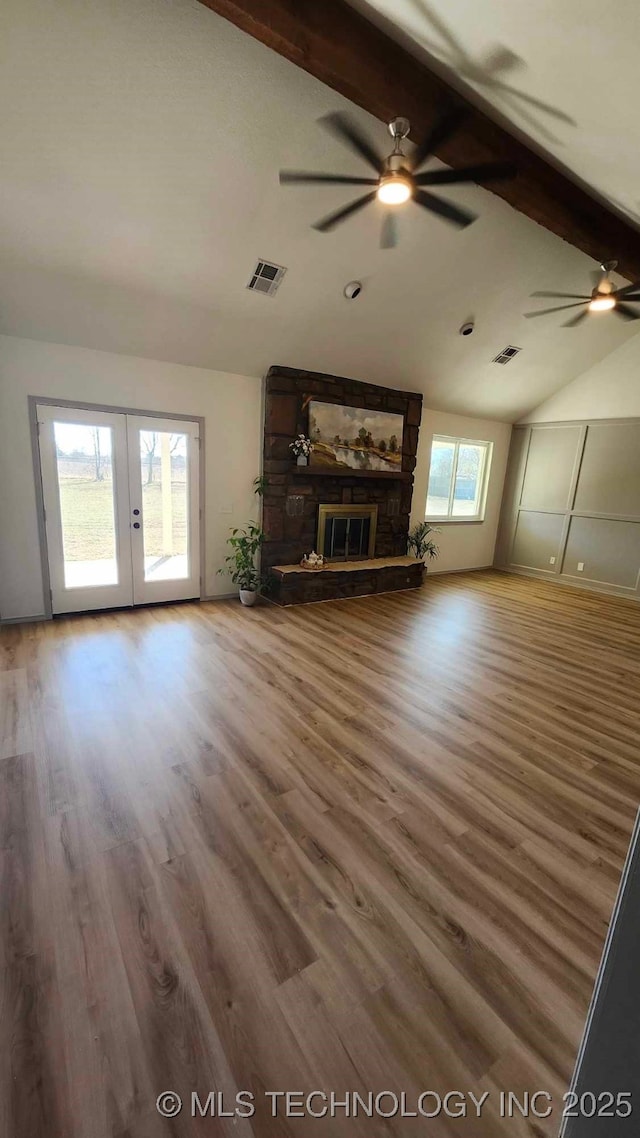 unfurnished living room with visible vents, wood finished floors, beamed ceiling, french doors, and a fireplace