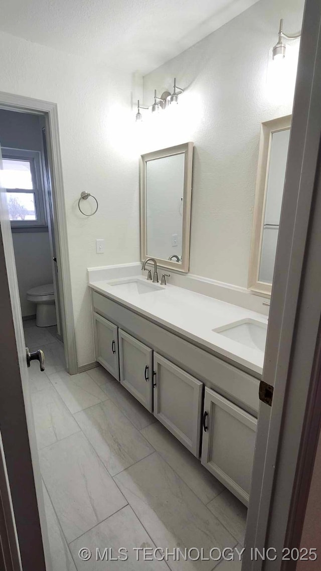 full bathroom featuring marble finish floor, a sink, toilet, and double vanity