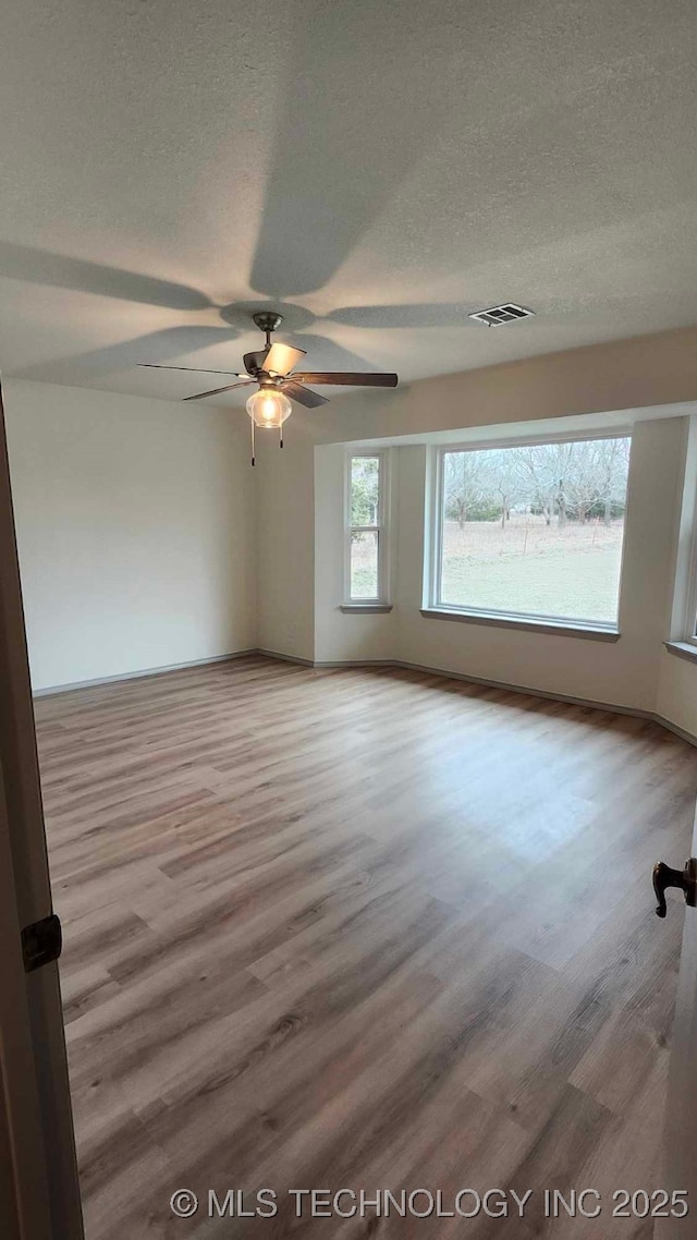 unfurnished room featuring a textured ceiling, ceiling fan, wood finished floors, and visible vents