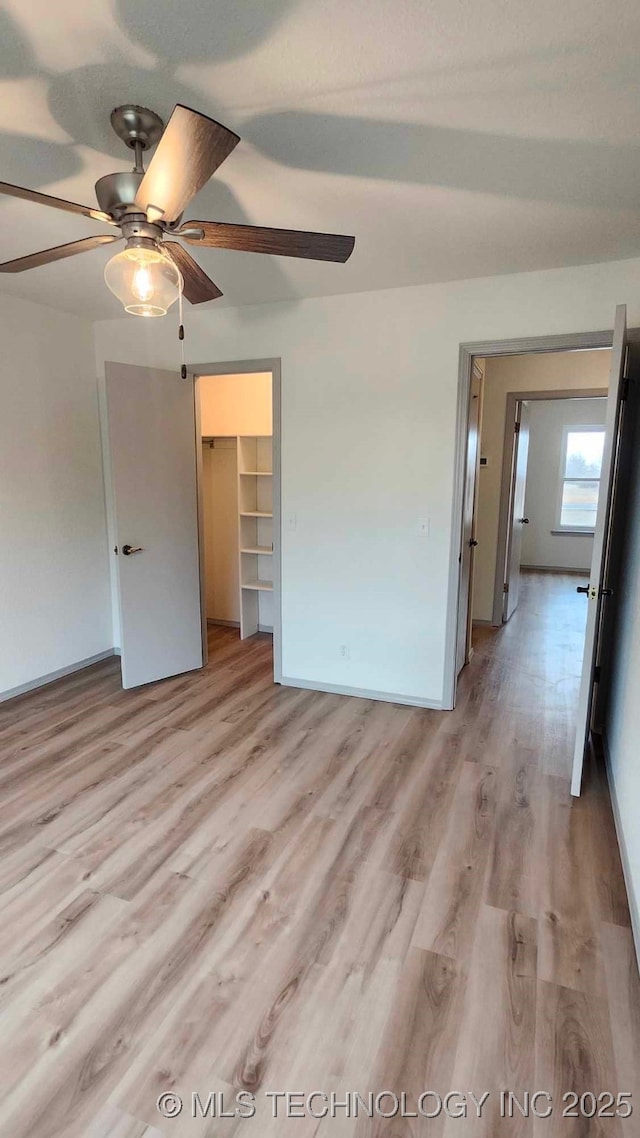 unfurnished bedroom with light wood-type flooring, a closet, a walk in closet, and a ceiling fan