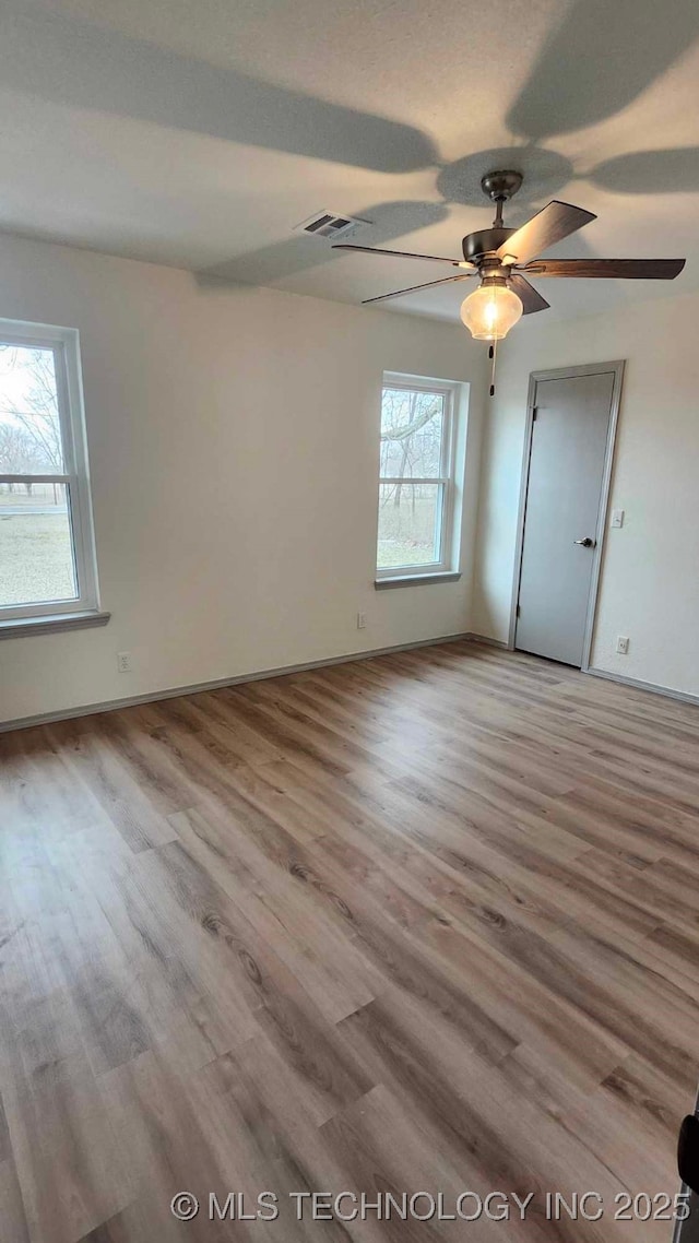 unfurnished room featuring baseboards, wood finished floors, visible vents, and a ceiling fan