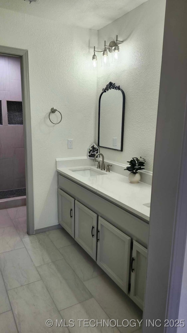 full bath with a textured wall, marble finish floor, tiled shower, and vanity